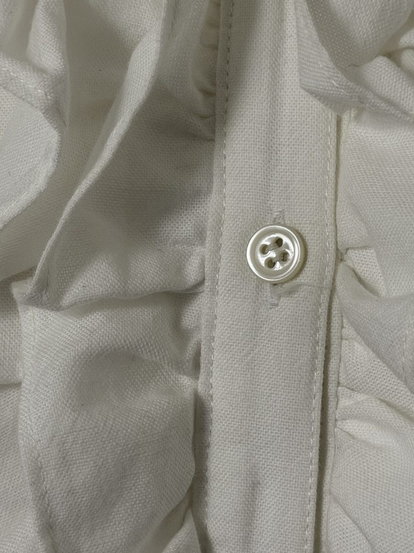 Close-up of mother-of-pearl button on the placket with frill alongside